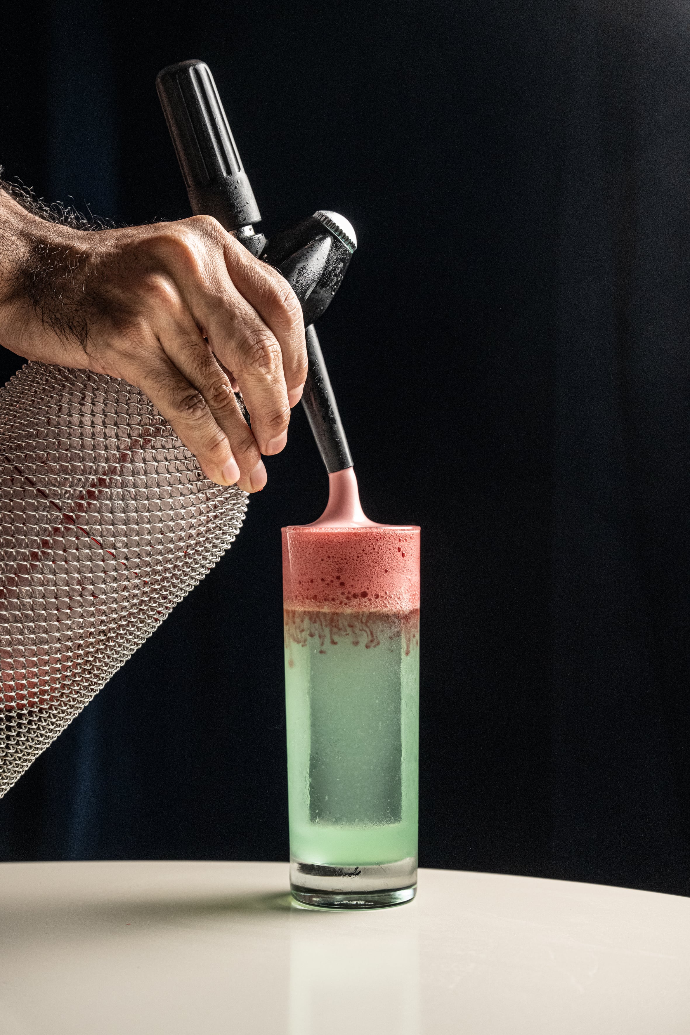 Bartender coronando con sifón un cóctel verde con espuma rosa