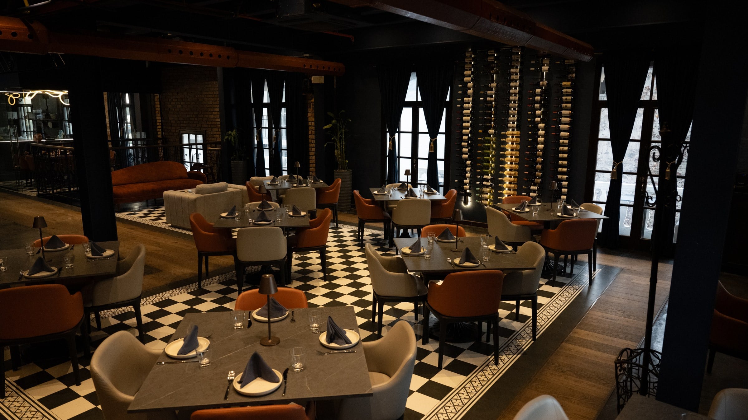Salón de Marula con suelo ajedrezado, sillas terracota y una pared de botellas iluminada al fondo