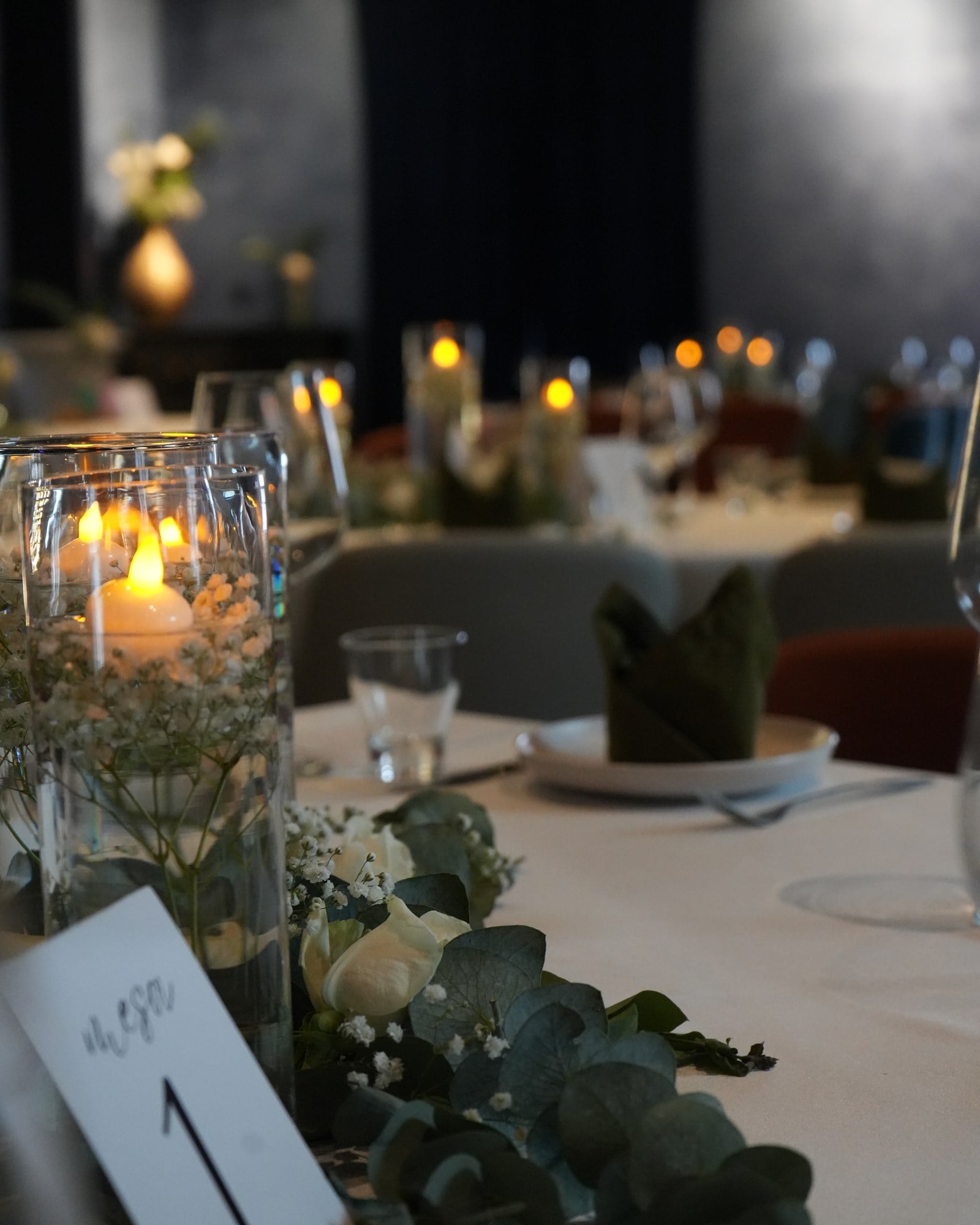 Detalle de un centro de mesa: velas flotantes en vasos de cristal entre rosas blancas y eucalipto